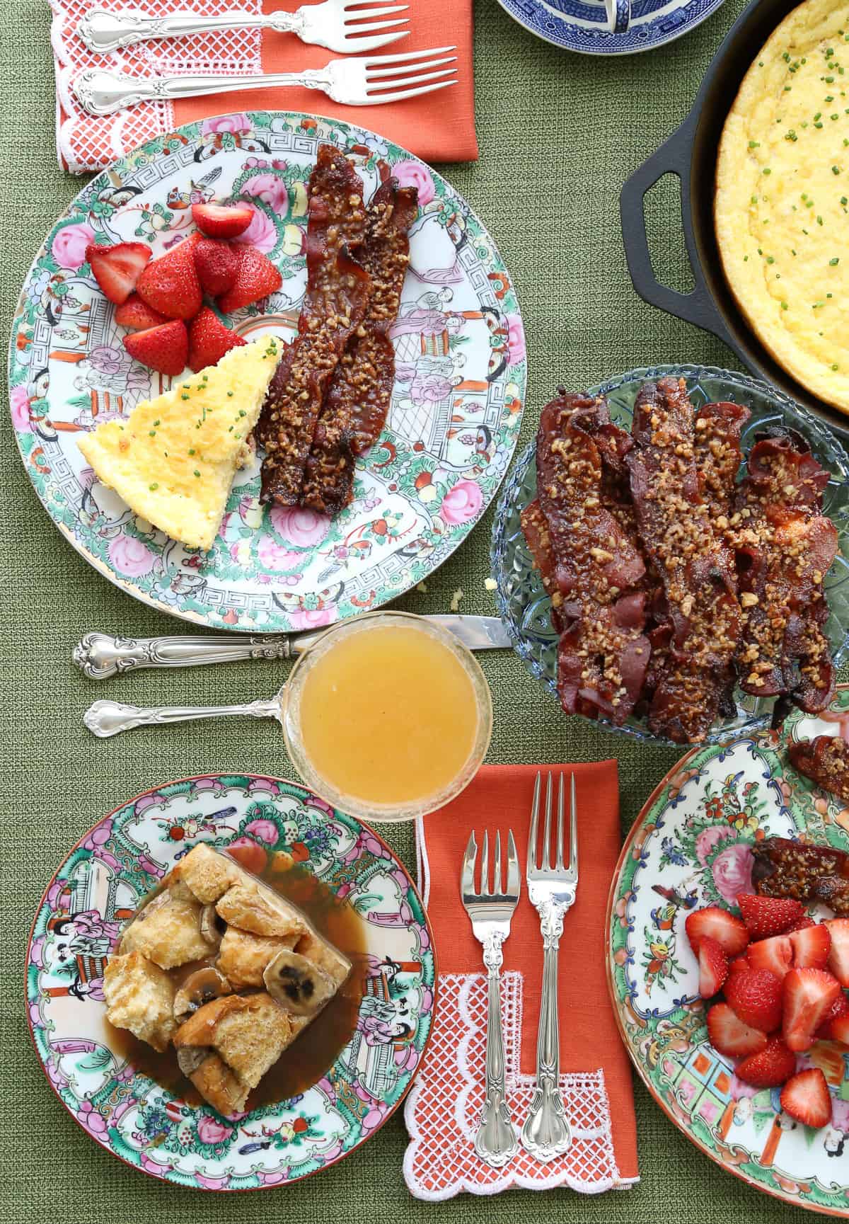 table set for brunch with berries, bacon, bellinis, and french toast casserole on china plates.