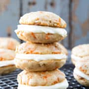 carrot cake whoopie pies with cream cheese frosting stacked on a wire rack.