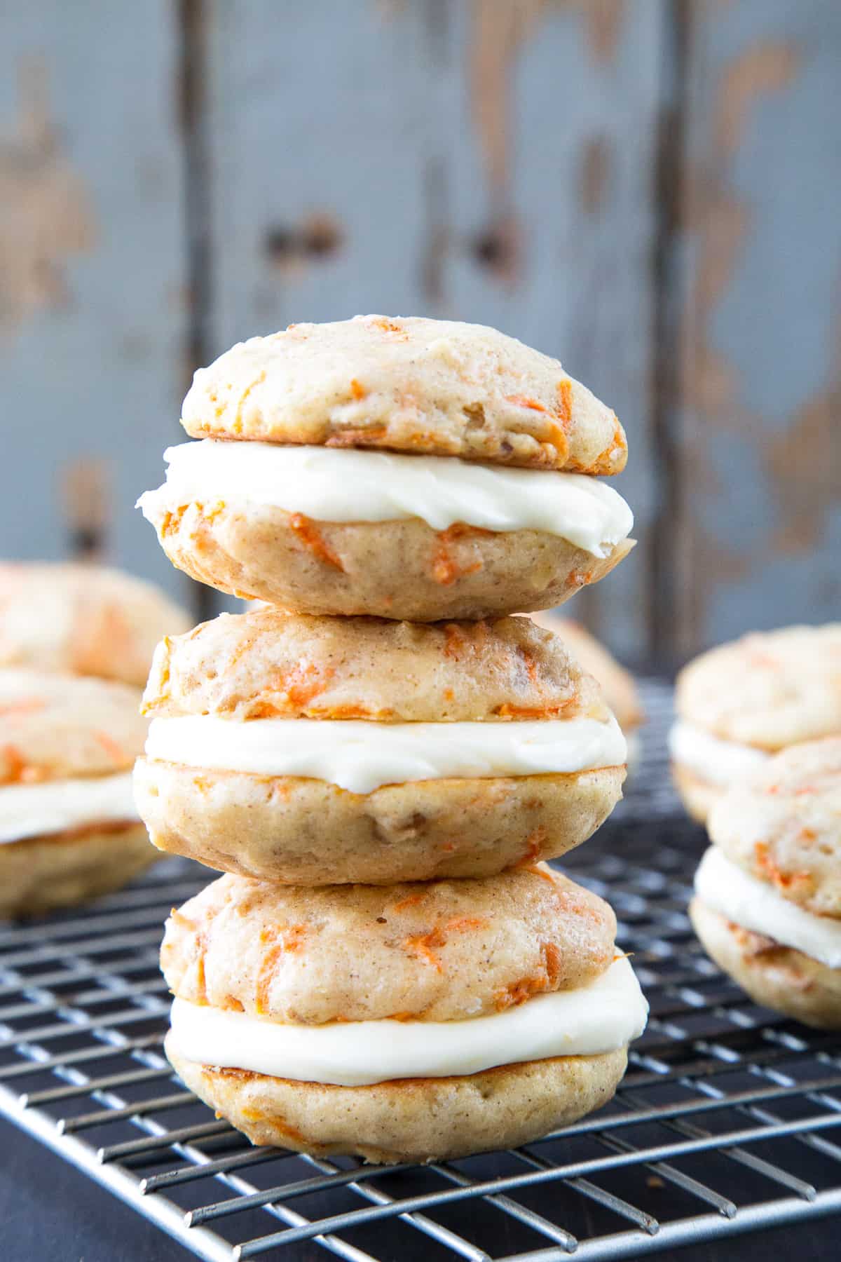 carrot cake whoopie pies with cream cheese frosting stacked on a wire rack.