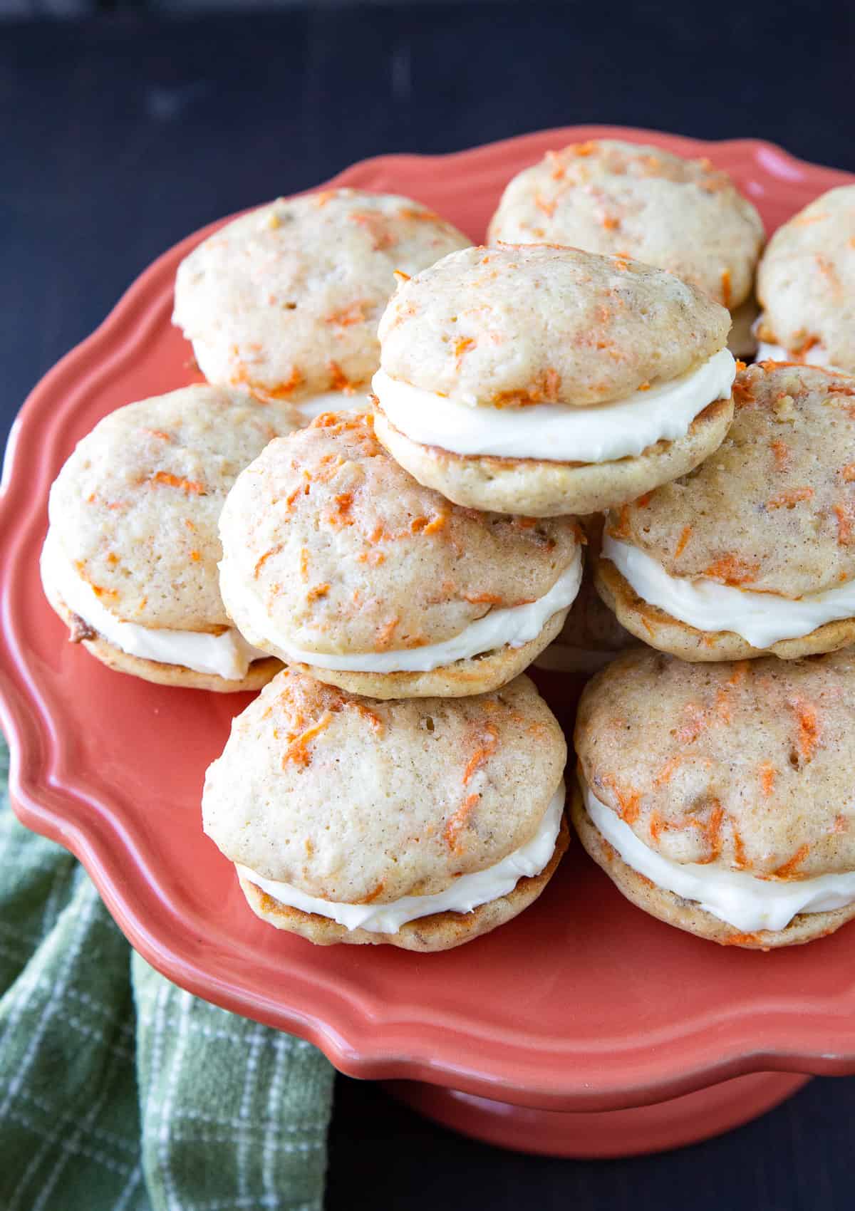 a pile of carrot cake whoopie pies on a pink cake pedestal.