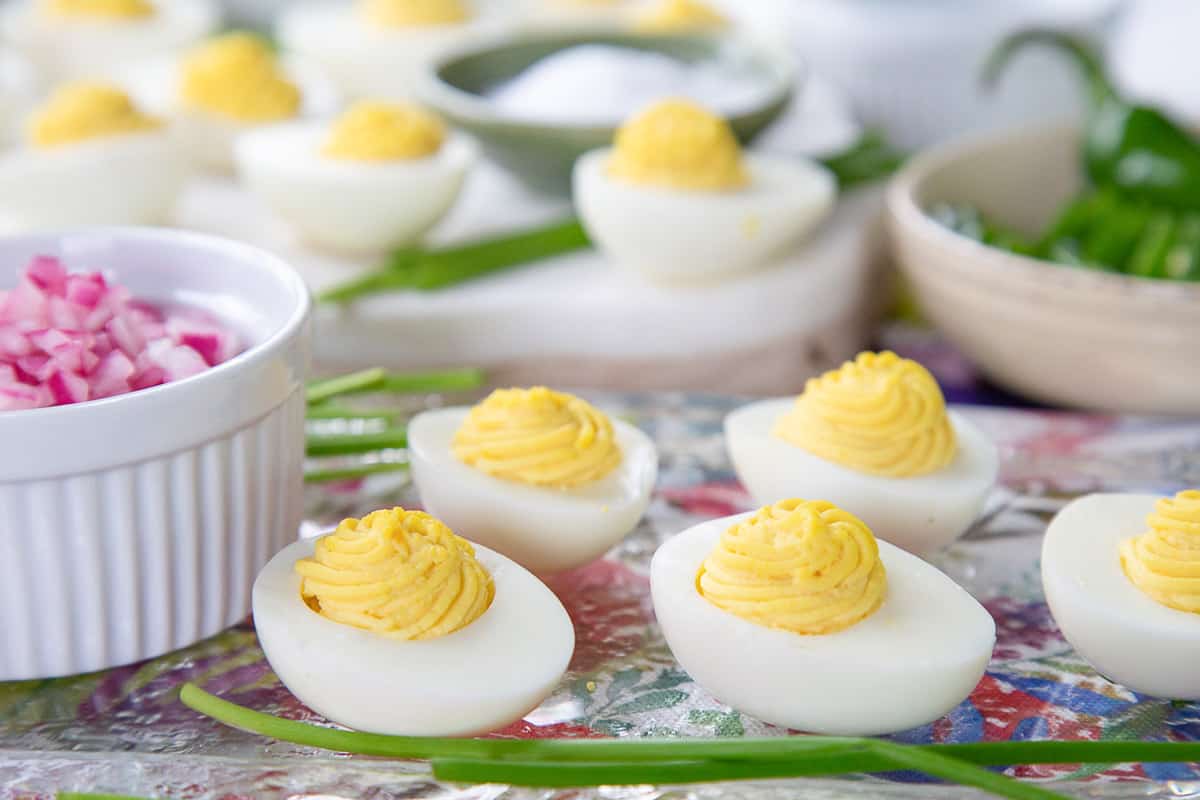 deviled eggs on a glass platter next to a ramekin of chopped red onion.