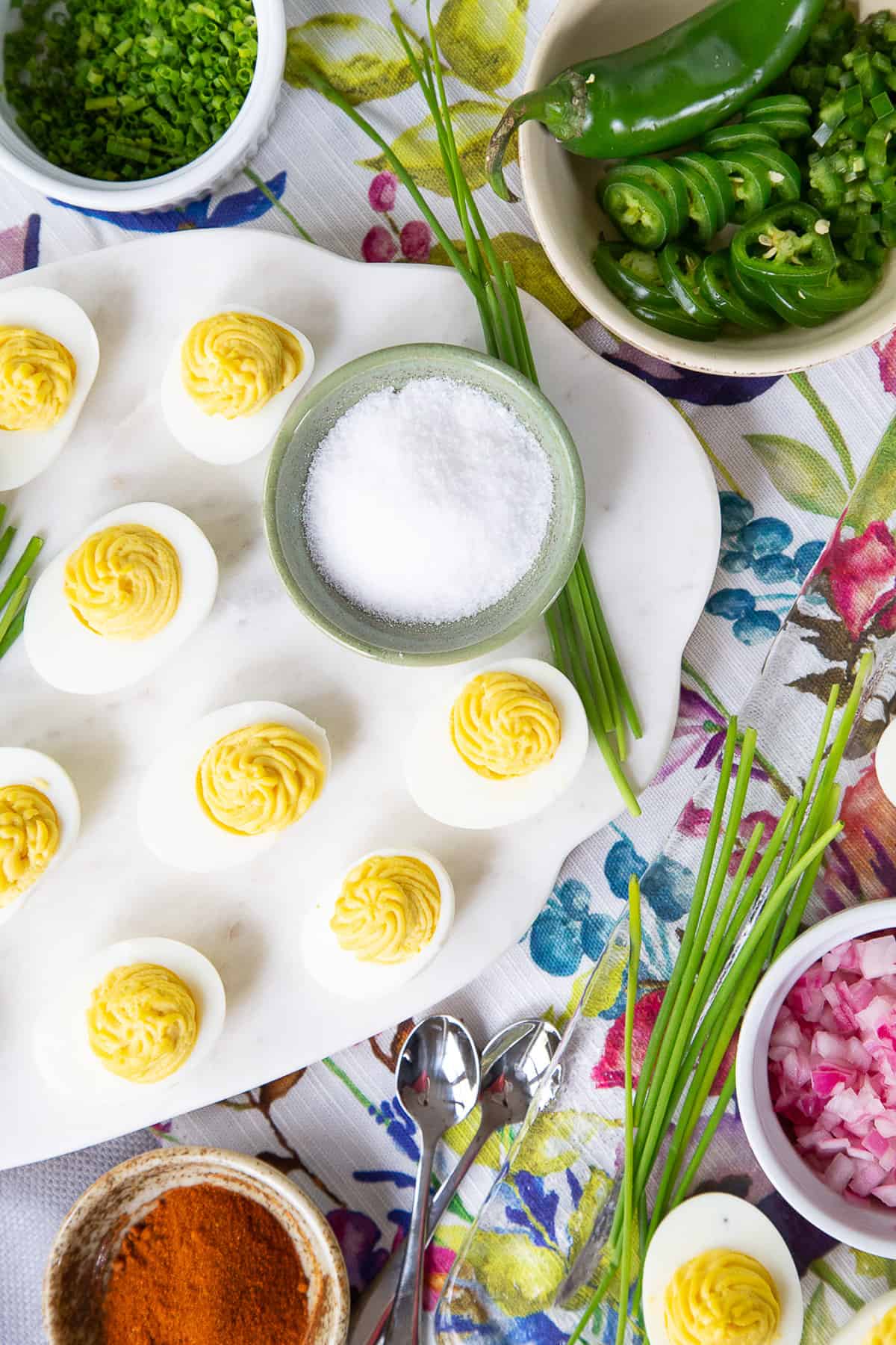 deviled eggs on a white platter with toppings scattered around them.