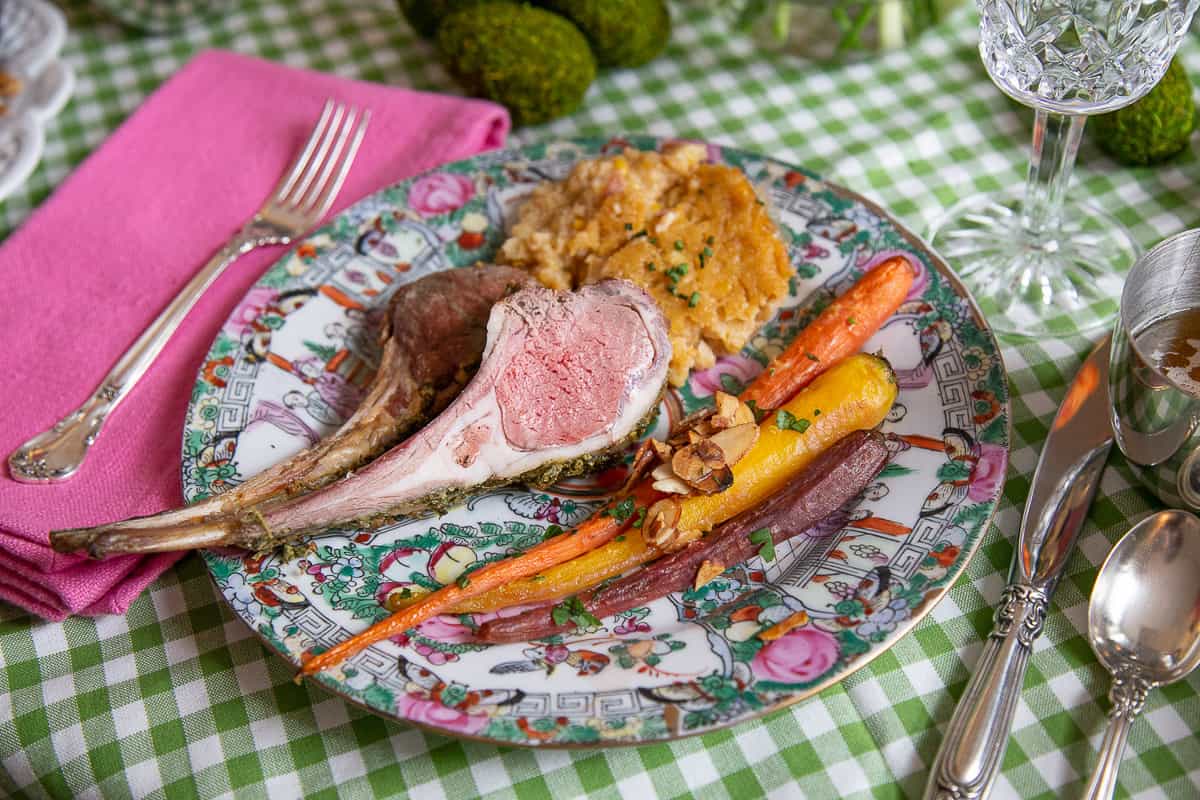 china plate with a lamb chop, roasted carrots, and corn casserole.