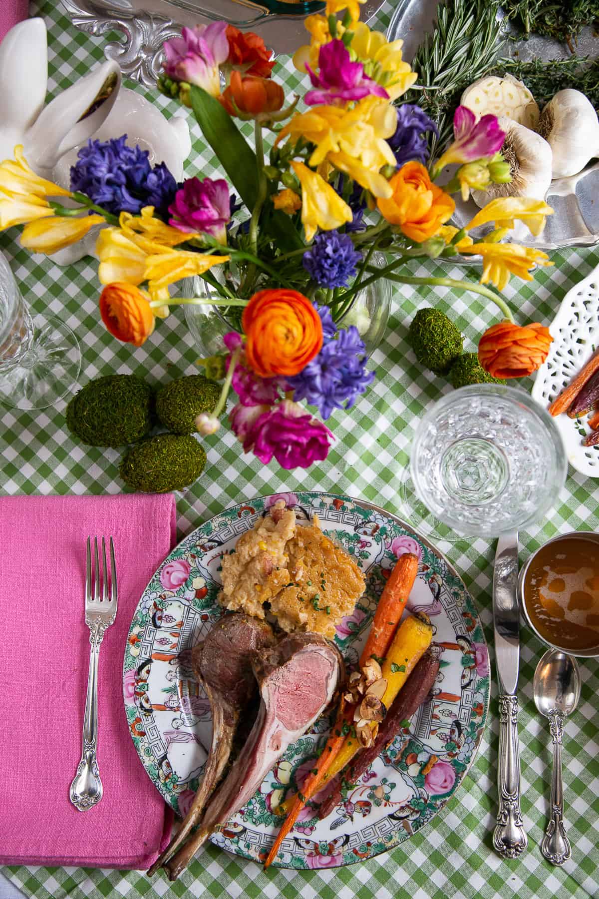 gingham tablecloth topped with a china plate of easter dinner and a vase of colorful flowers.