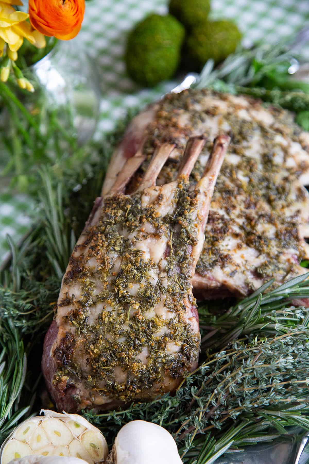 herb crusted rack of lamb on a platter with fresh herbs.