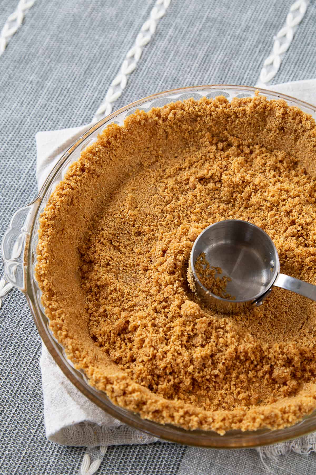 graham cracker crumbs in a pie plate being pushed down with a measuring cup.