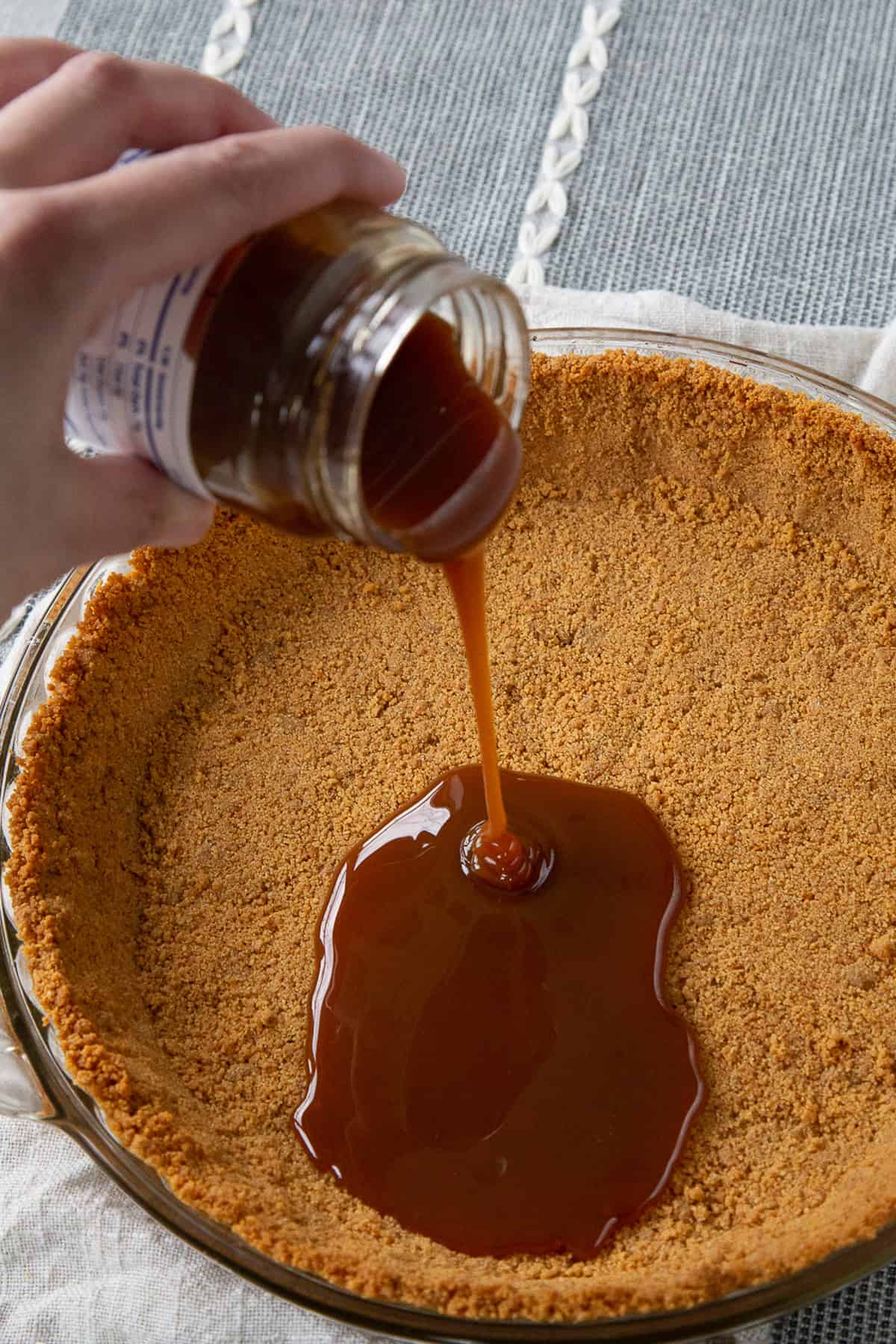 hand pouring caramel on a graham cracker crust.