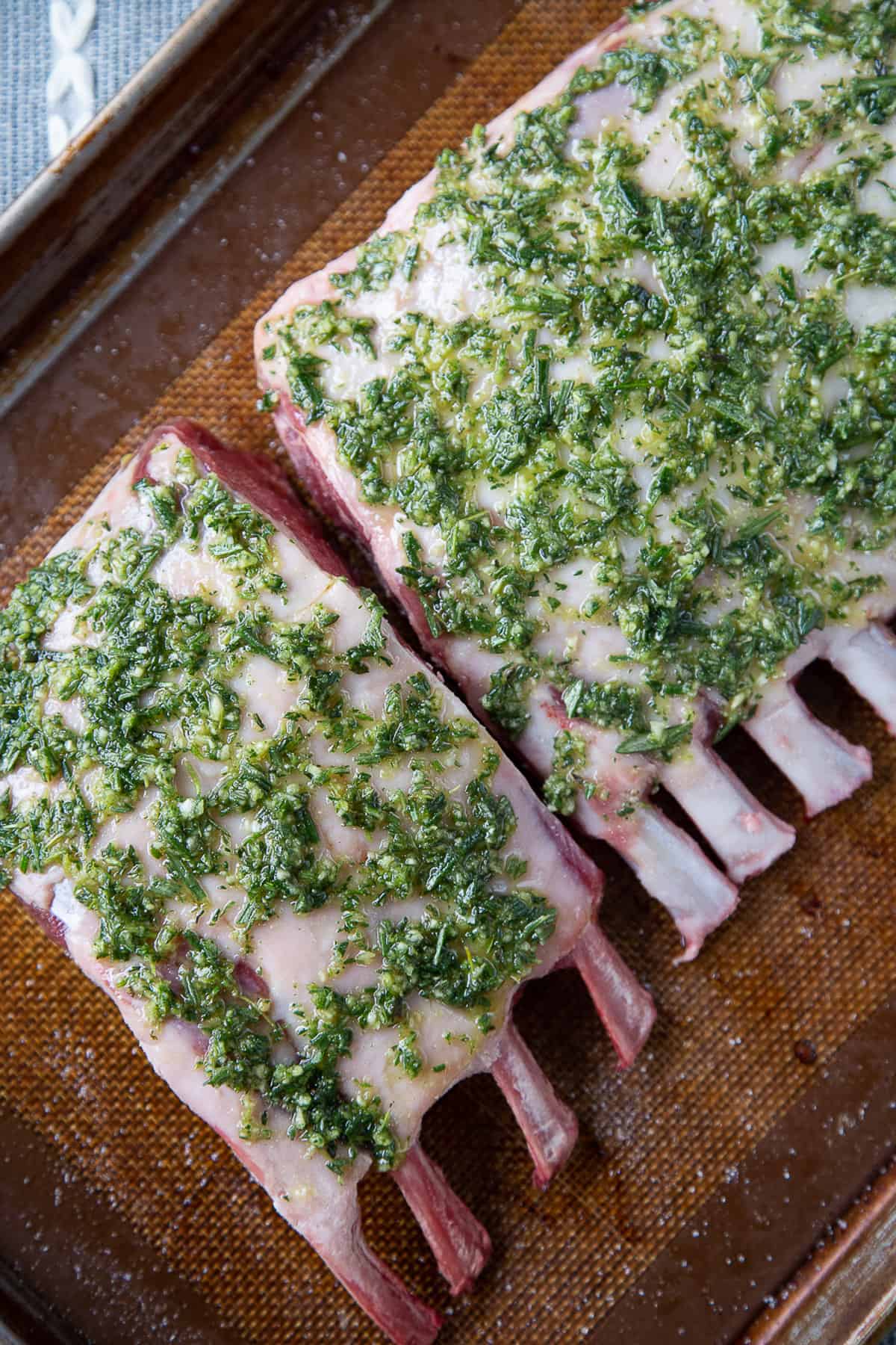 raw frenched rack of lamb on a baking sheet, topped with fresh herbs.