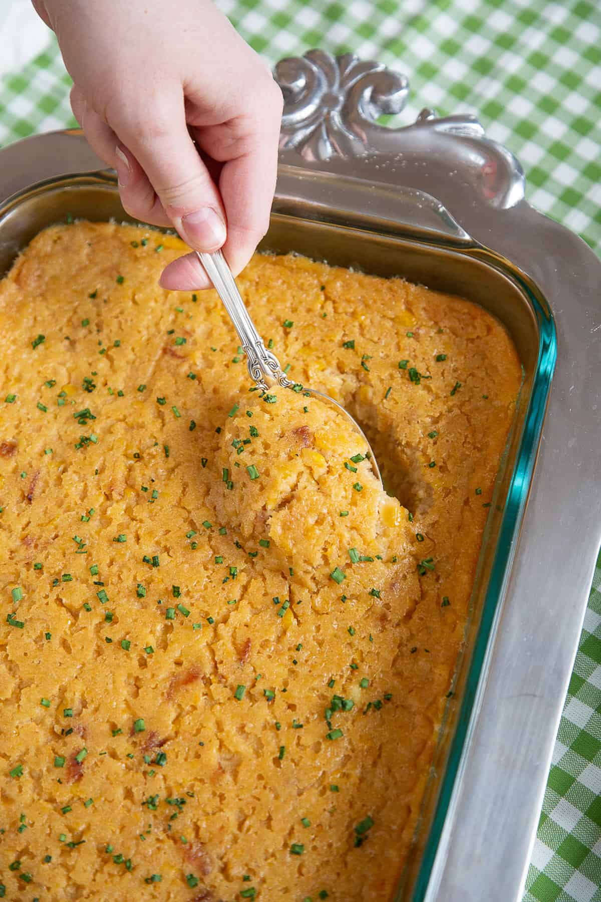 hand lifting a spoonful of scalloped corn out of a casserole dish.