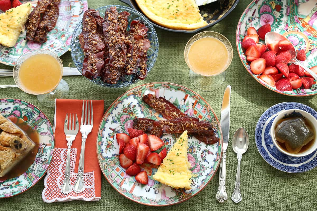 table set for brunch with colorful china, silverware, bacon, spoon bread, and strawberries.