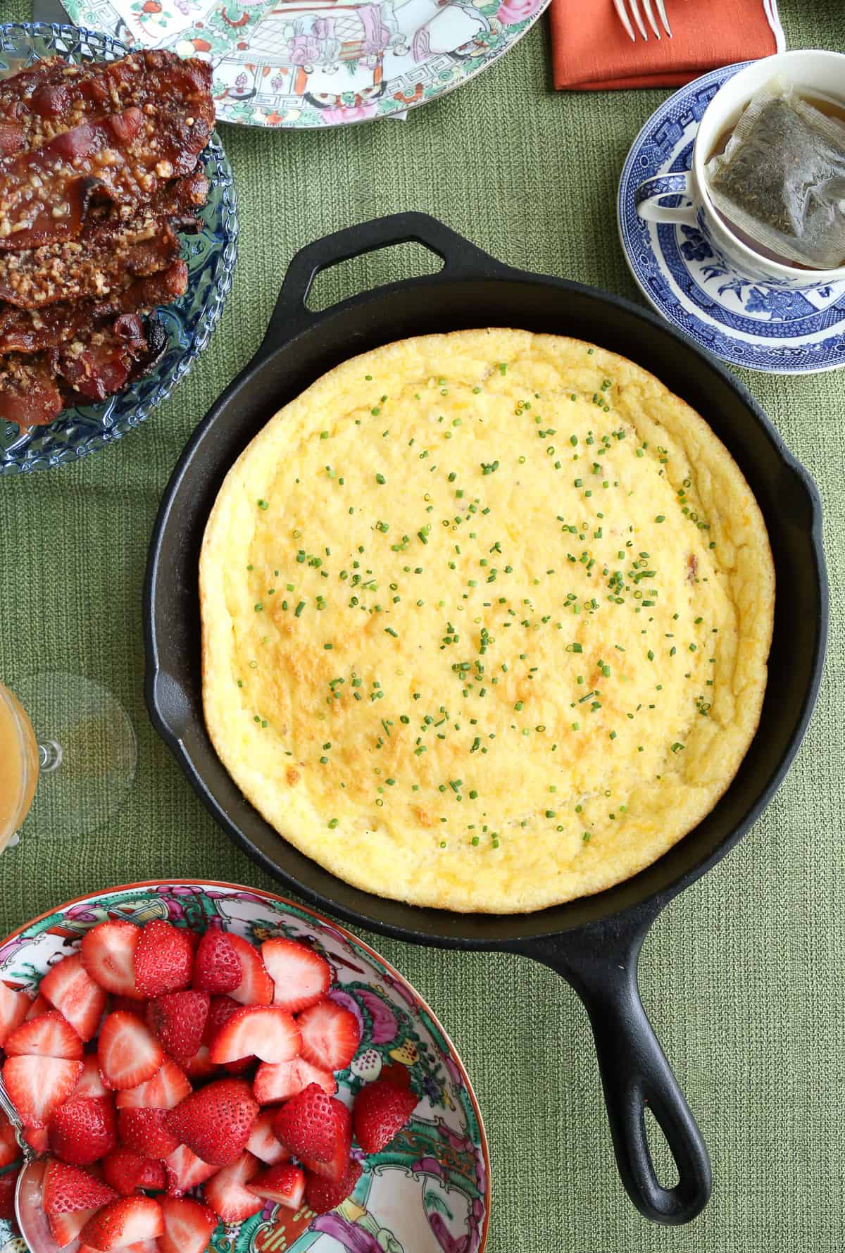 bacon cheddar spoon bread in a cast iron skillet on a green tablecloth.
