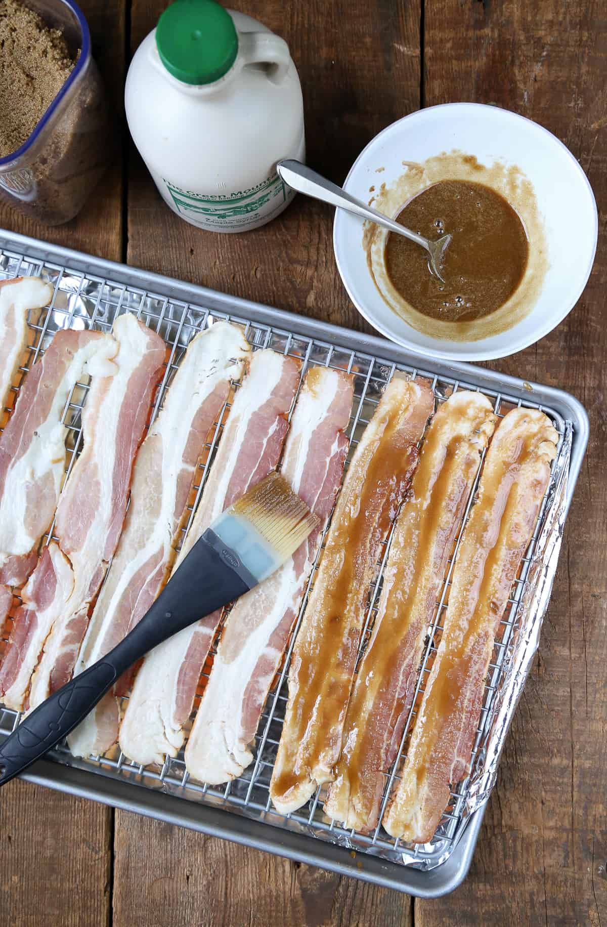 uncooked bacon on a sheet pan being brushed with a brown sugar mixture.