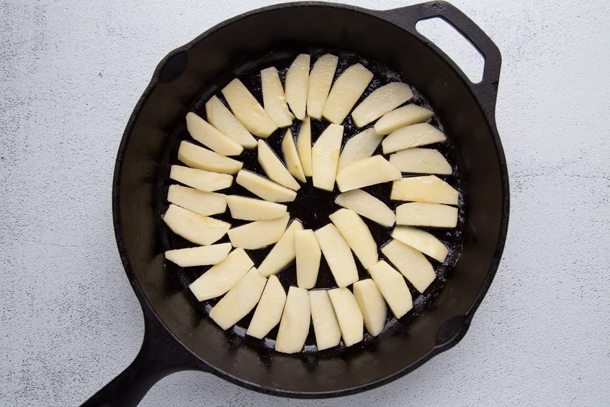 peeled apple slices fanned out in a cast iron skillet.