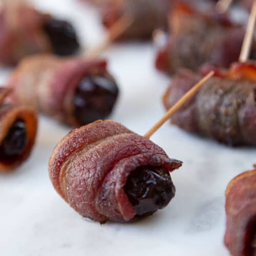 bacon wrapped dates with toothpicks on a white platter.