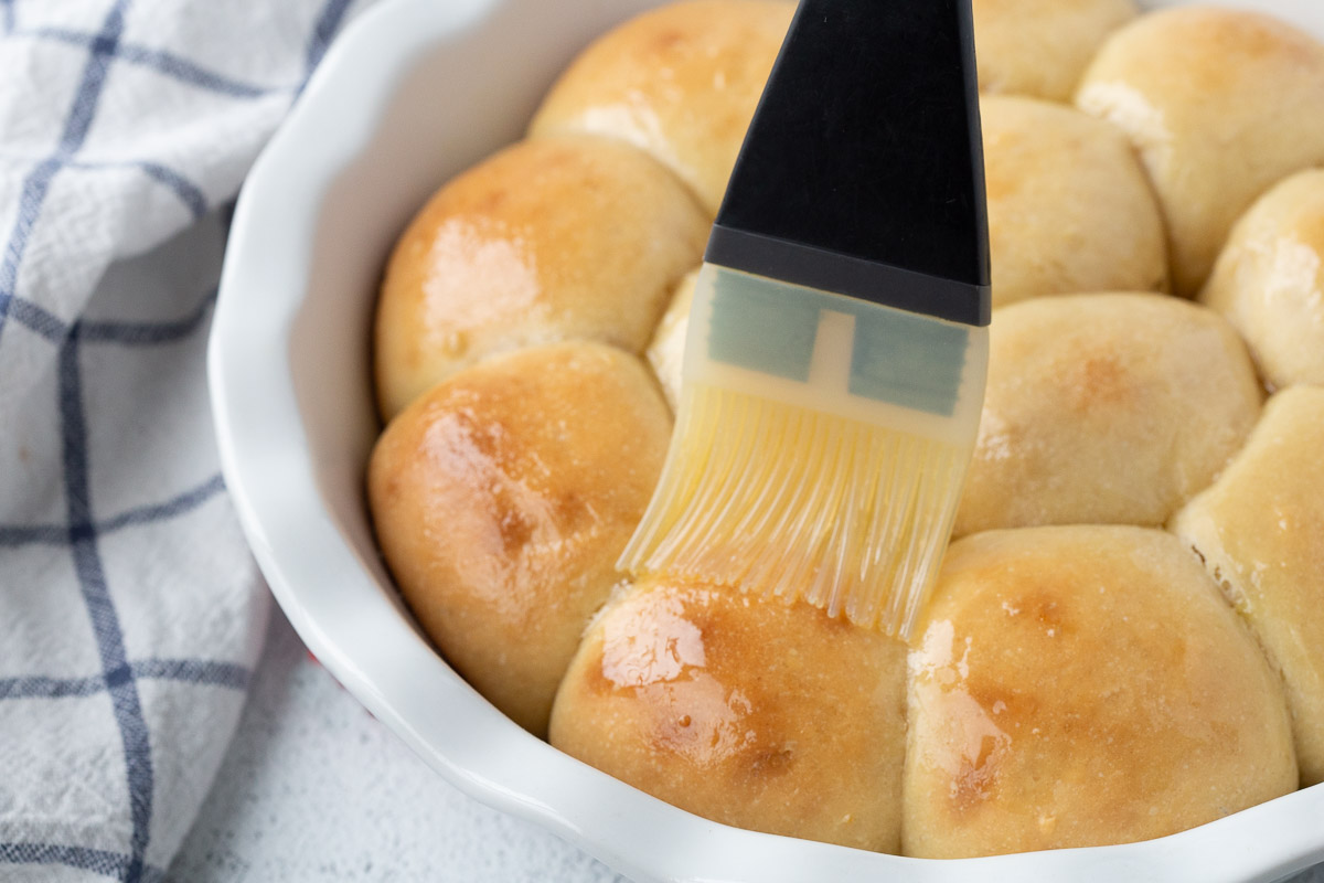 pastry brush brushing potato rolls with butter.