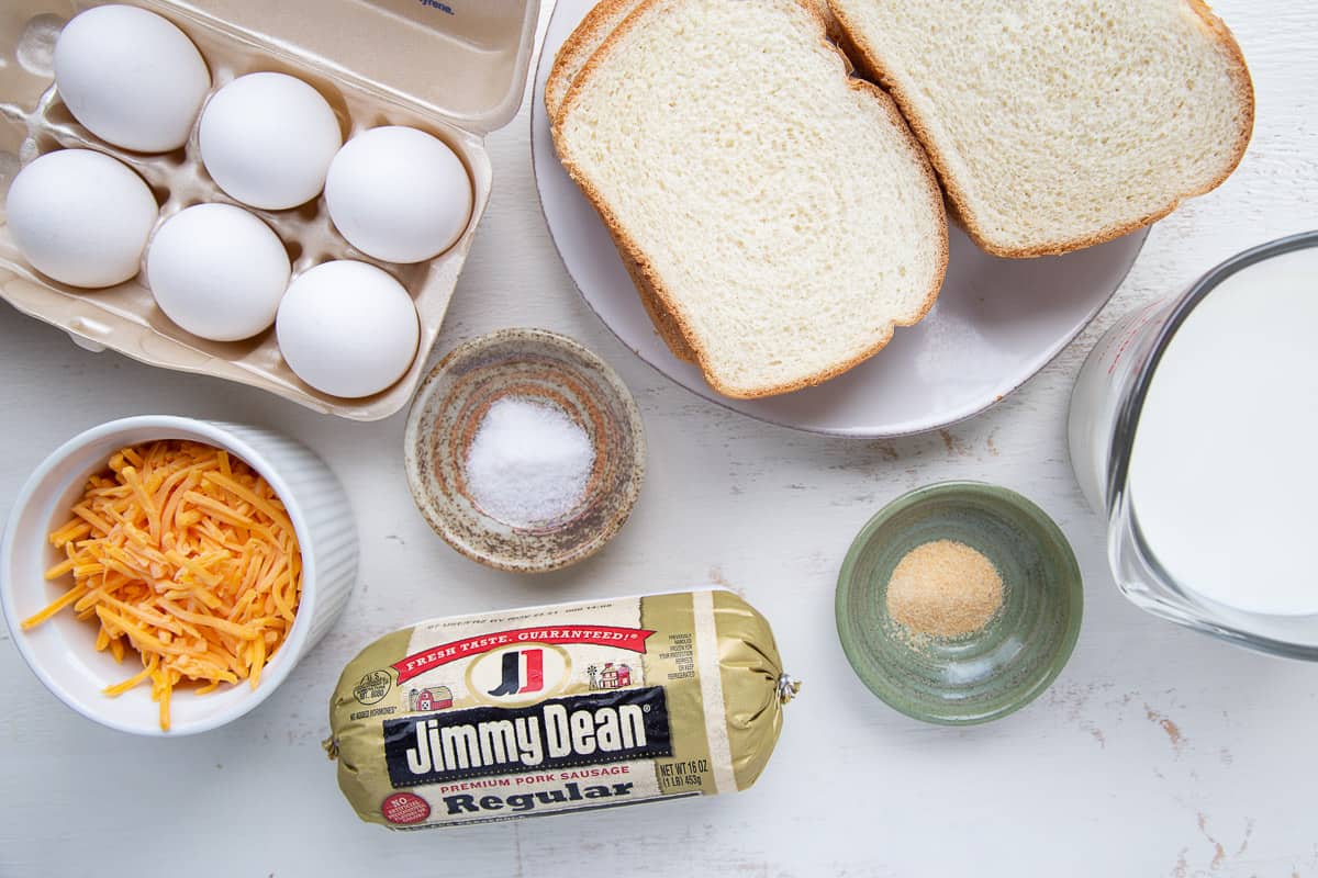 bread, eggs, sausage, and other casserole ingredients on a white table.