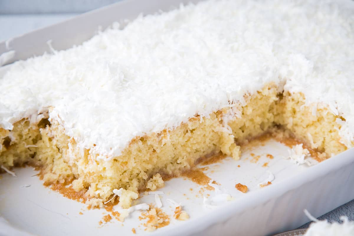 coconut poke cake with slices taken out in a white casserole dish.