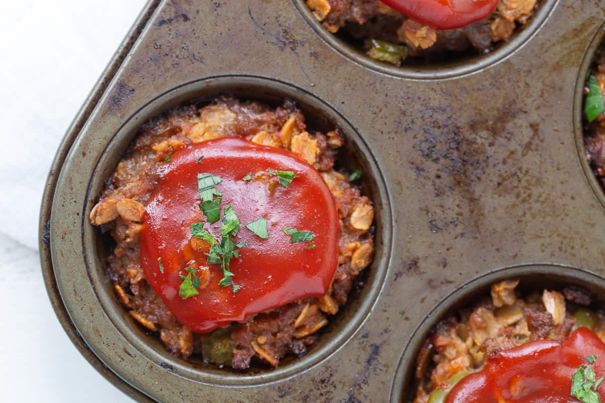 mini meatloaves topped with ketchup in a muffin tin.