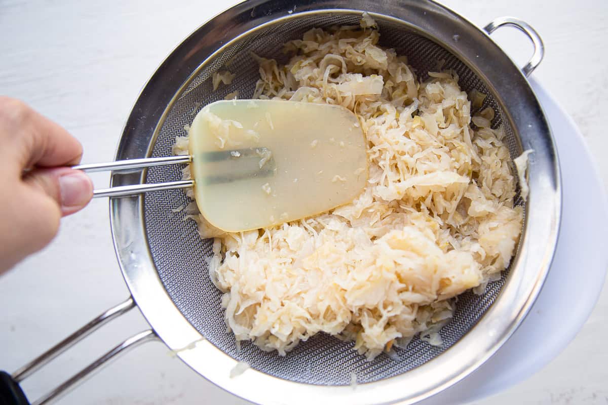 spatula pressing sauerkraut in a colander.