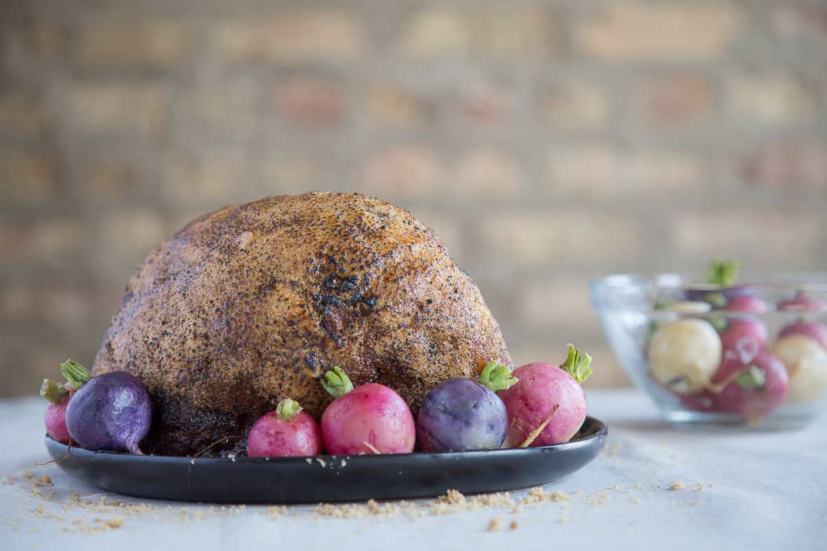 glazed ham on a black platter with rainbow radishes.