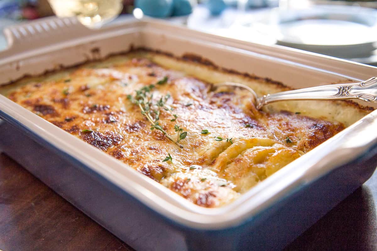 spoon in a blue casserole dish filled with gruyere scalloped potatoes.
