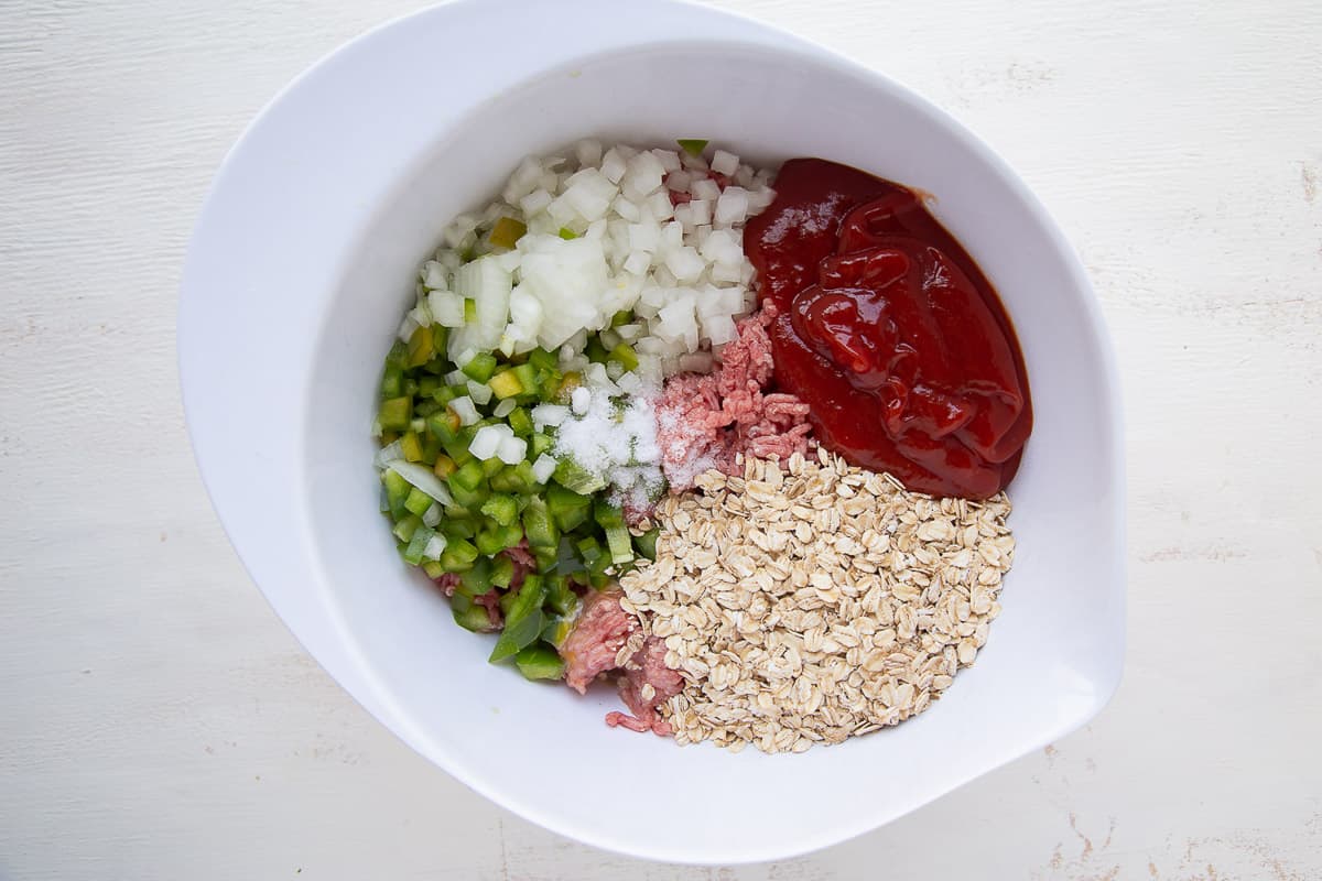 ground beef, oats, ketchup, and diced veggies in a white bowl.