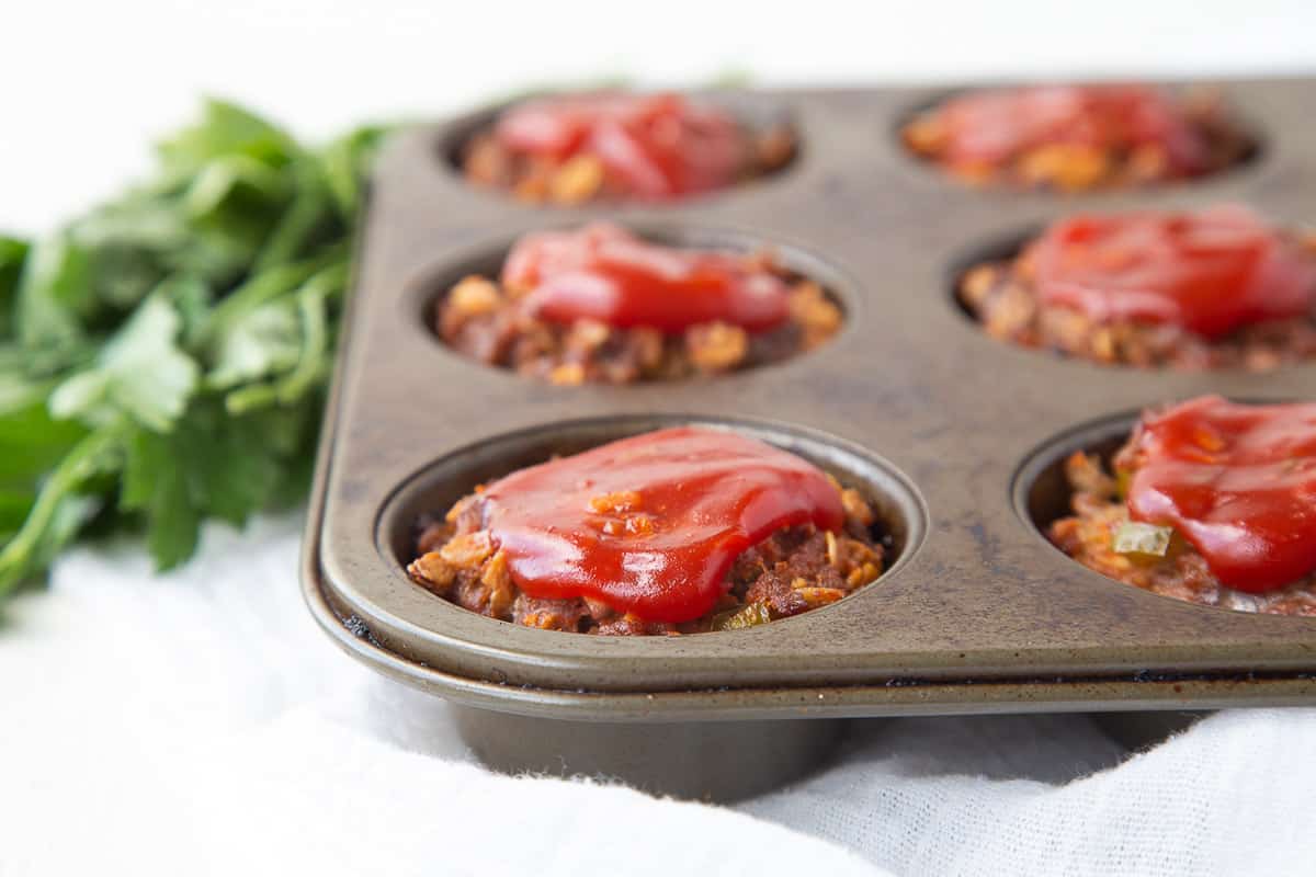 meatloaves in a muffin tin topped with ketchup.