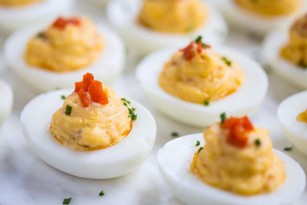 deviled eggs topped with pimentos on a white platter.