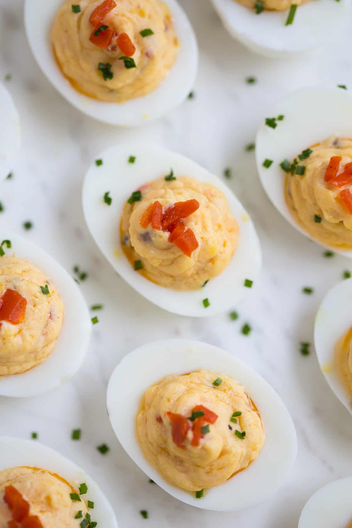 pimento cheese deviled eggs on a white platter, topped with chives.