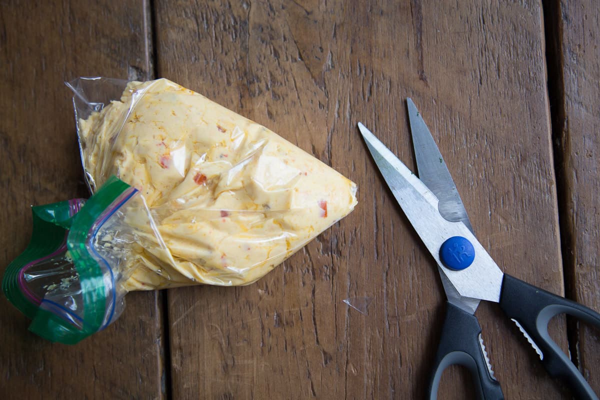 piping bag filled with pimento cheese and a pair of scissors on a wooden table.