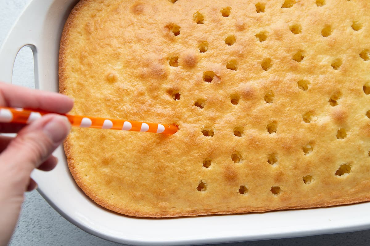 drinking straw poking holes in a white cake.