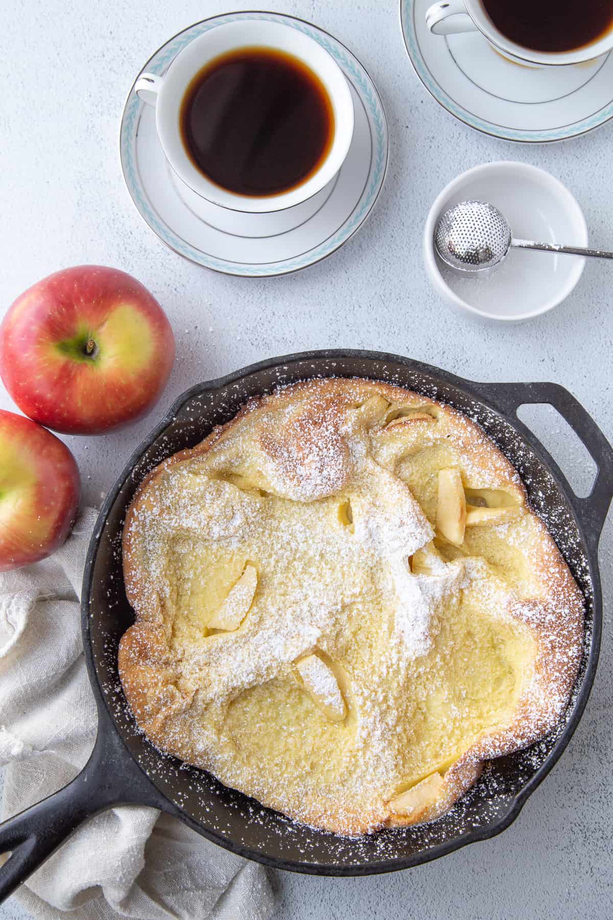 german pancake with apple in a cast iron skillet next to a cup of coffee.