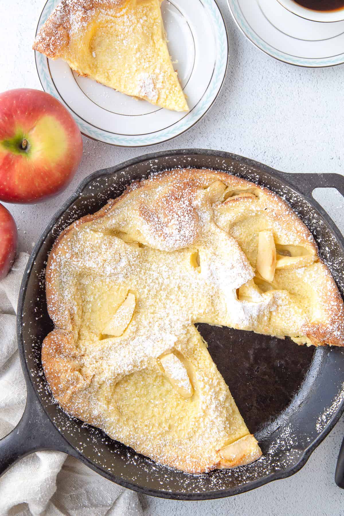 german pancake with apples in a cast iron skillet with a slice taken out.