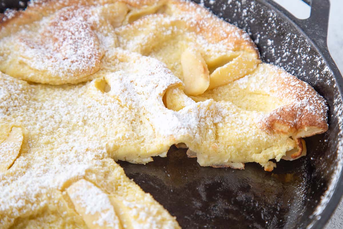 german pancake with apples in a cast iron skillet with a slice taken out.