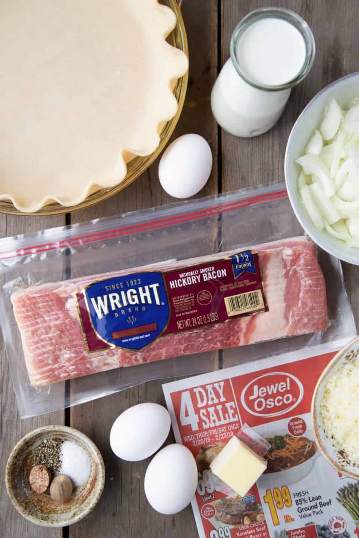 bacon, pie crust, eggs, milk, and other ingredients on a wooden table.