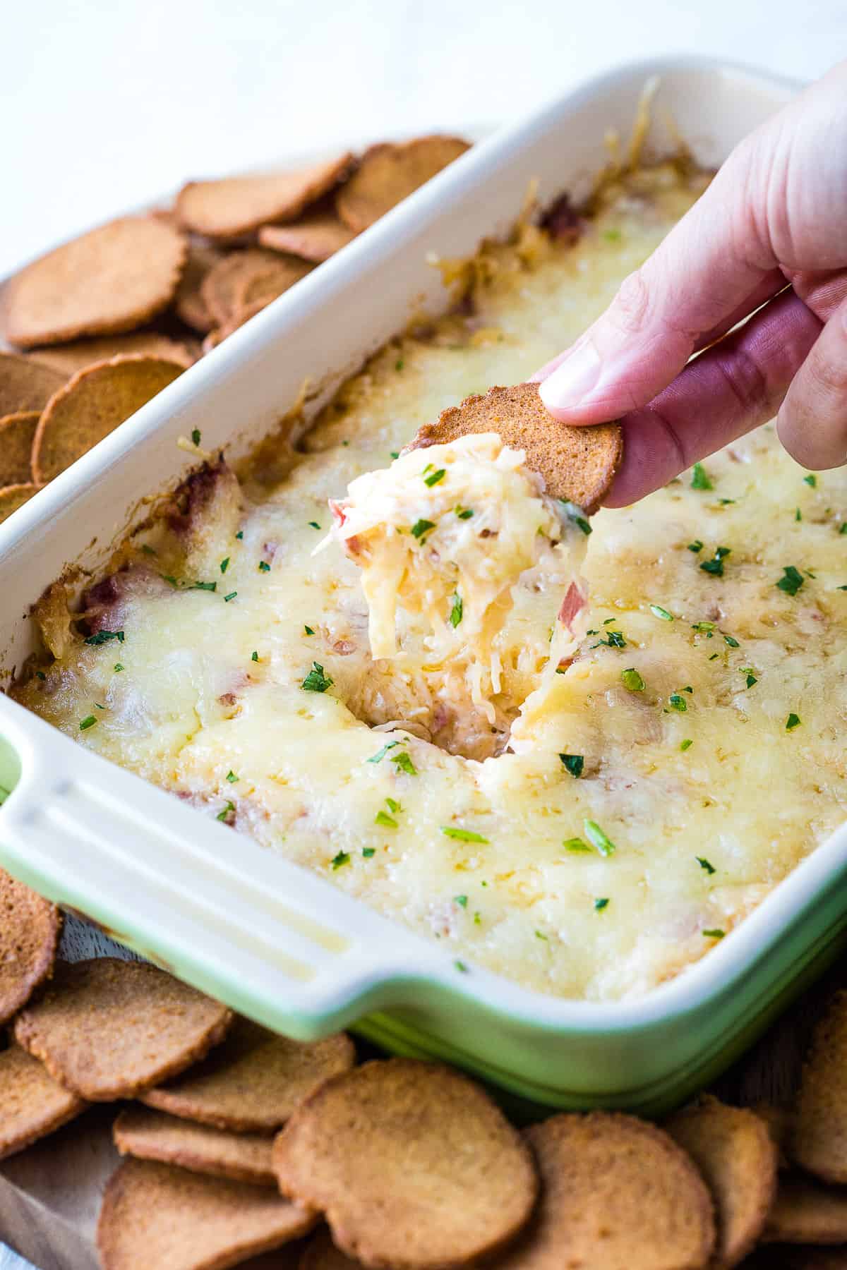 hand scooping up reuben dip with a rye cracker.