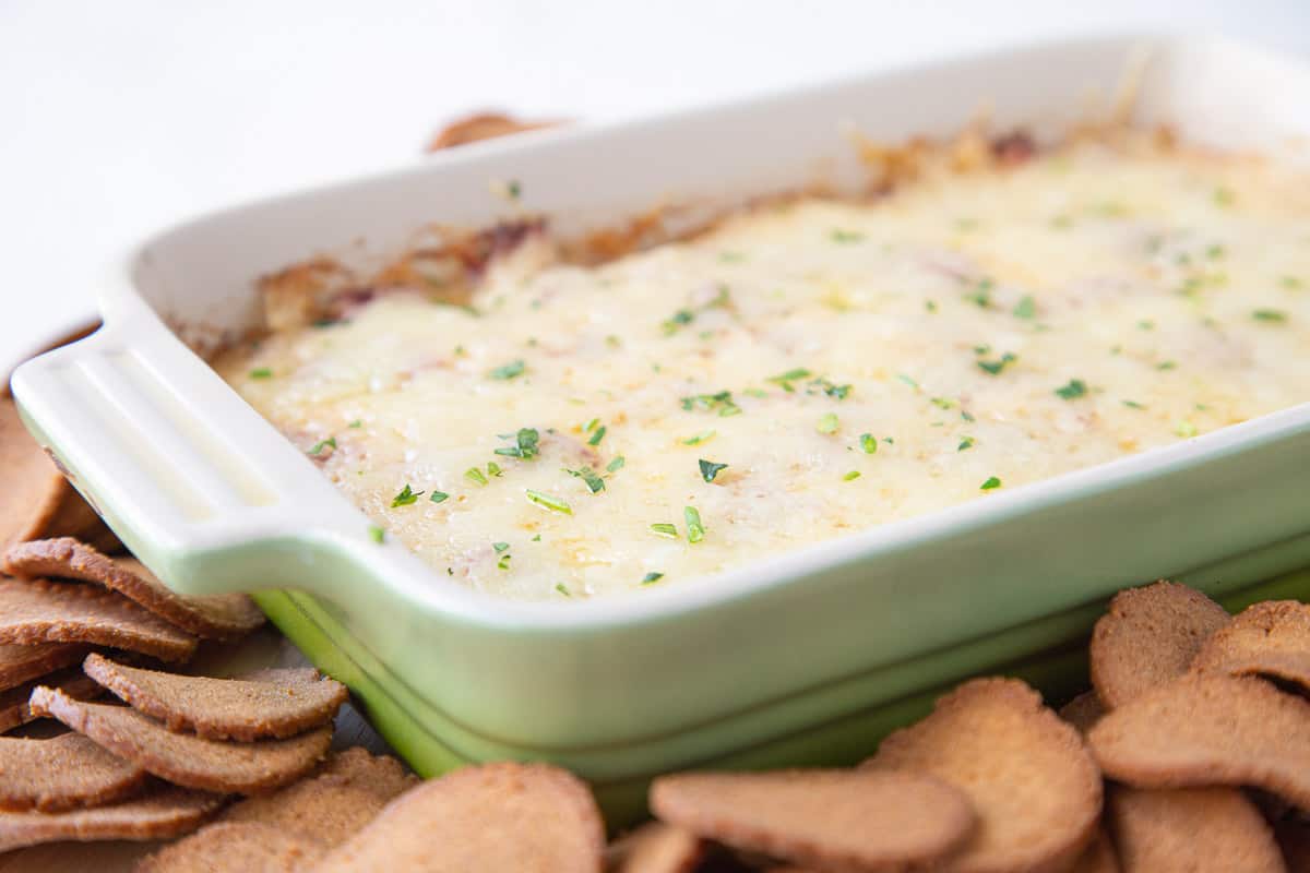 cooked reuben dip covered with cheese in a green casserole dish.