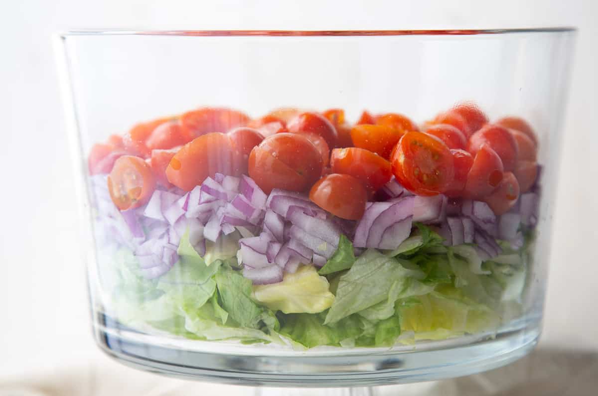 lettuce, red onion, and tomatoes in a glass trifle dish.