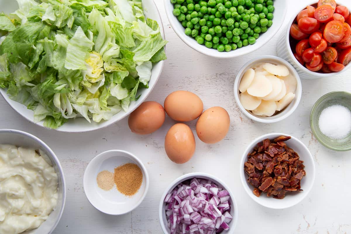 lettuce, eggs, peas, red onion, and other ingredients on a white table.