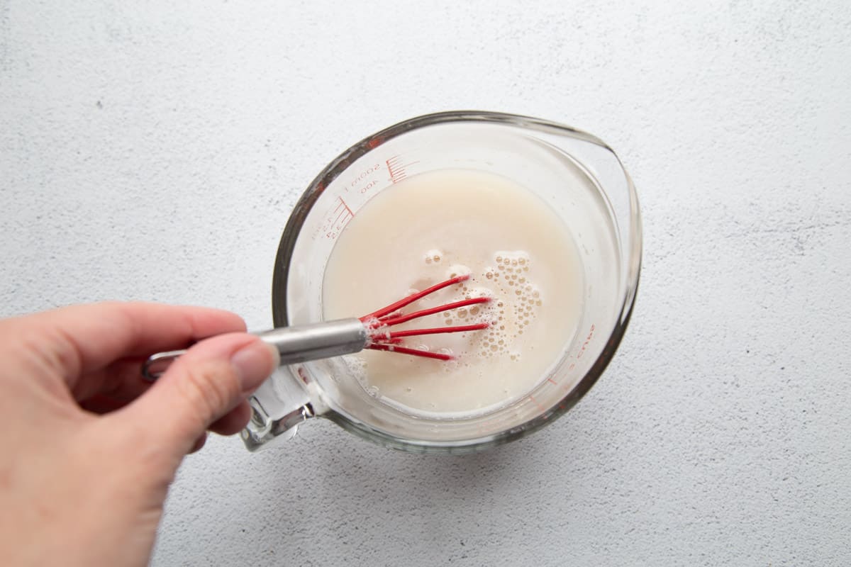 hand whisking yeast into a glass measuring cup of water.