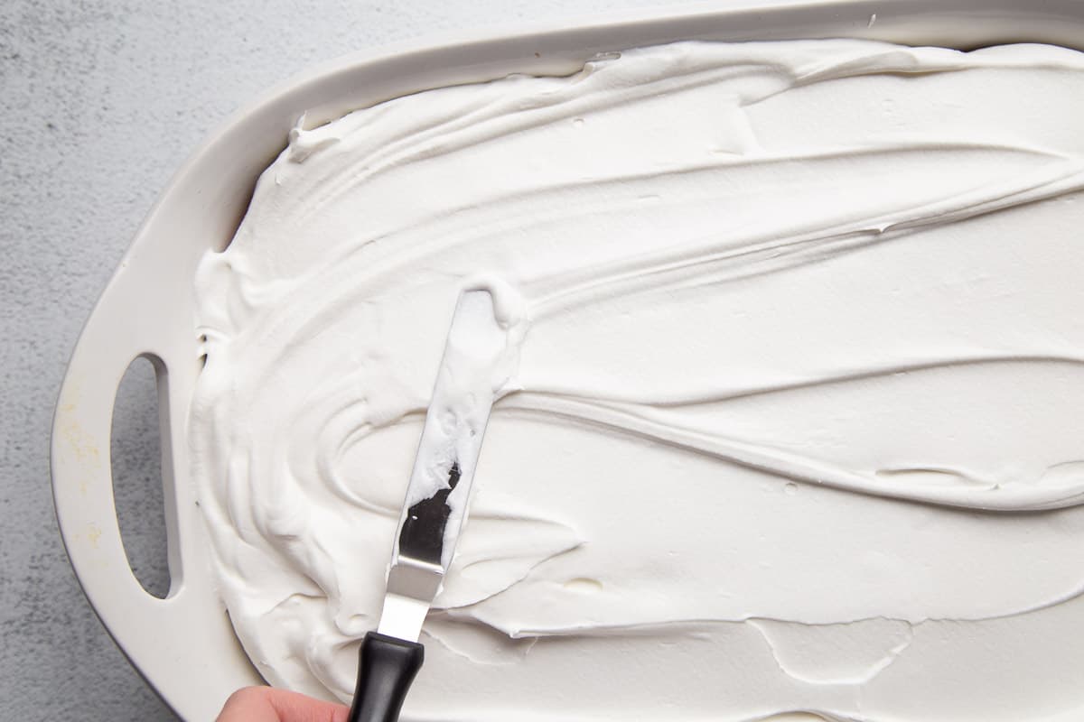 hand using an offset spatula to spread whipped cream on a cake.