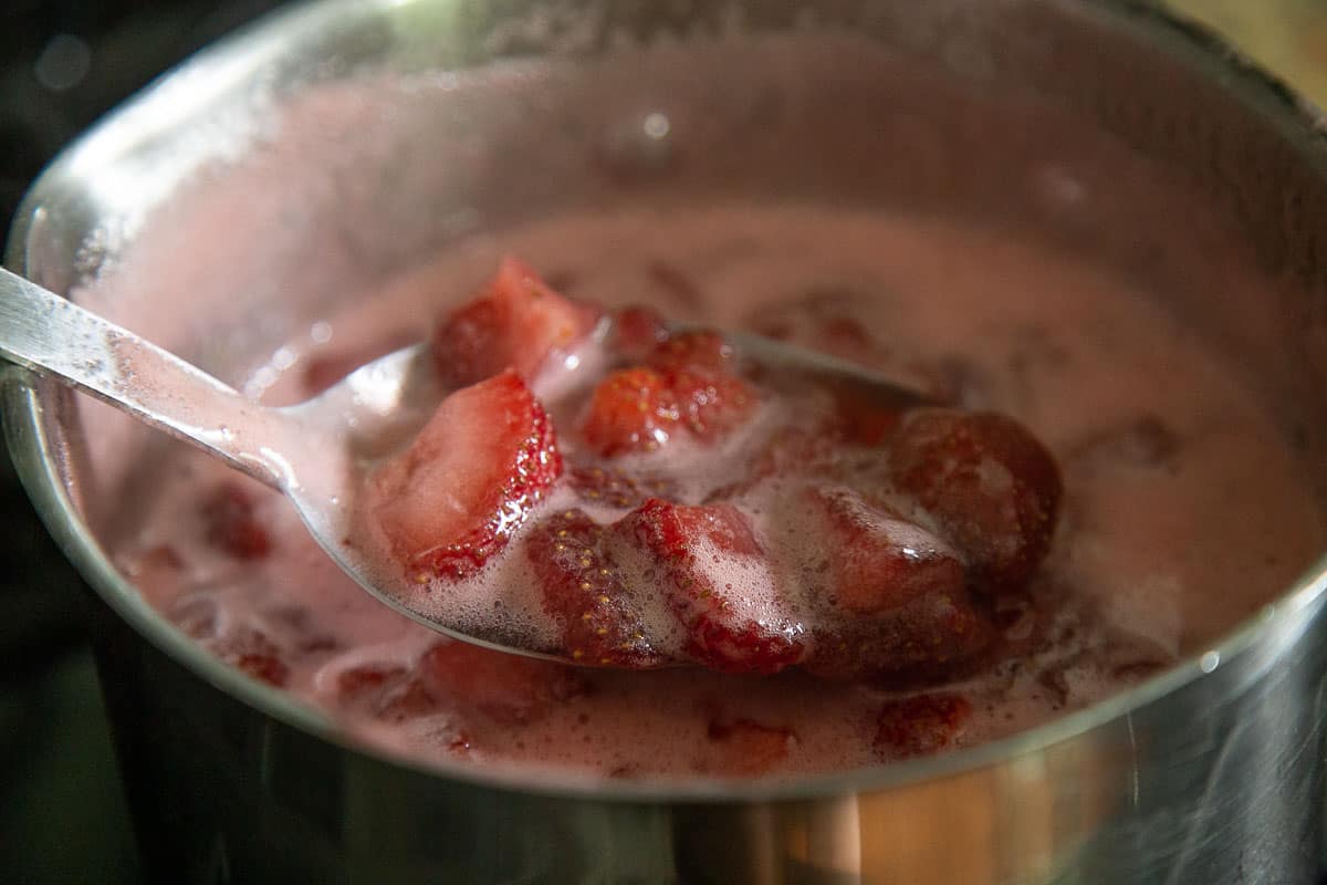 a spoon lifting strawberries out of a saucepan.