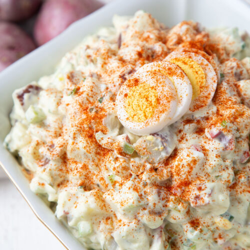 red potato salad topped with hard boiled eggs and paprika in a white dish.