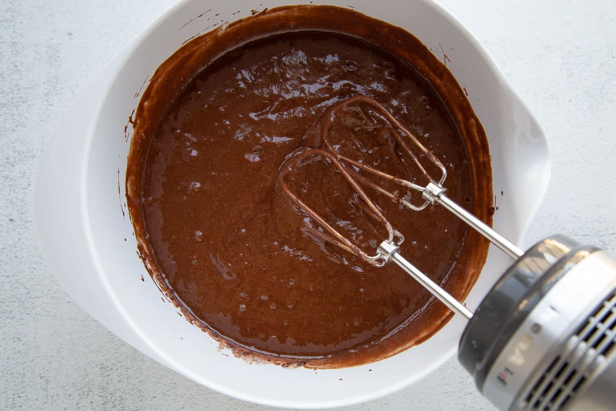 chocolate cake batter in a white bowl with a hand mixer.