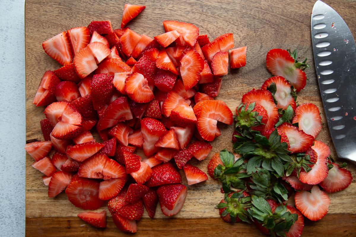 chopped strawberries on a wooden cutting board.