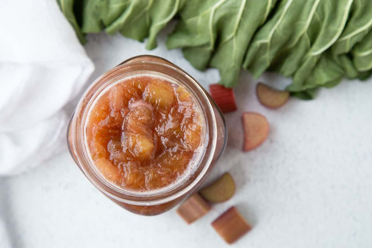 rhubarb sauce in a glass jar next to rhubarb leaves.