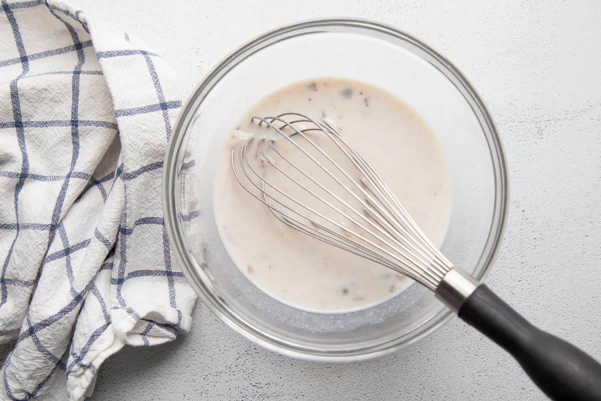 cream of mushroom soup and milk in a glass bowl with a whisk.