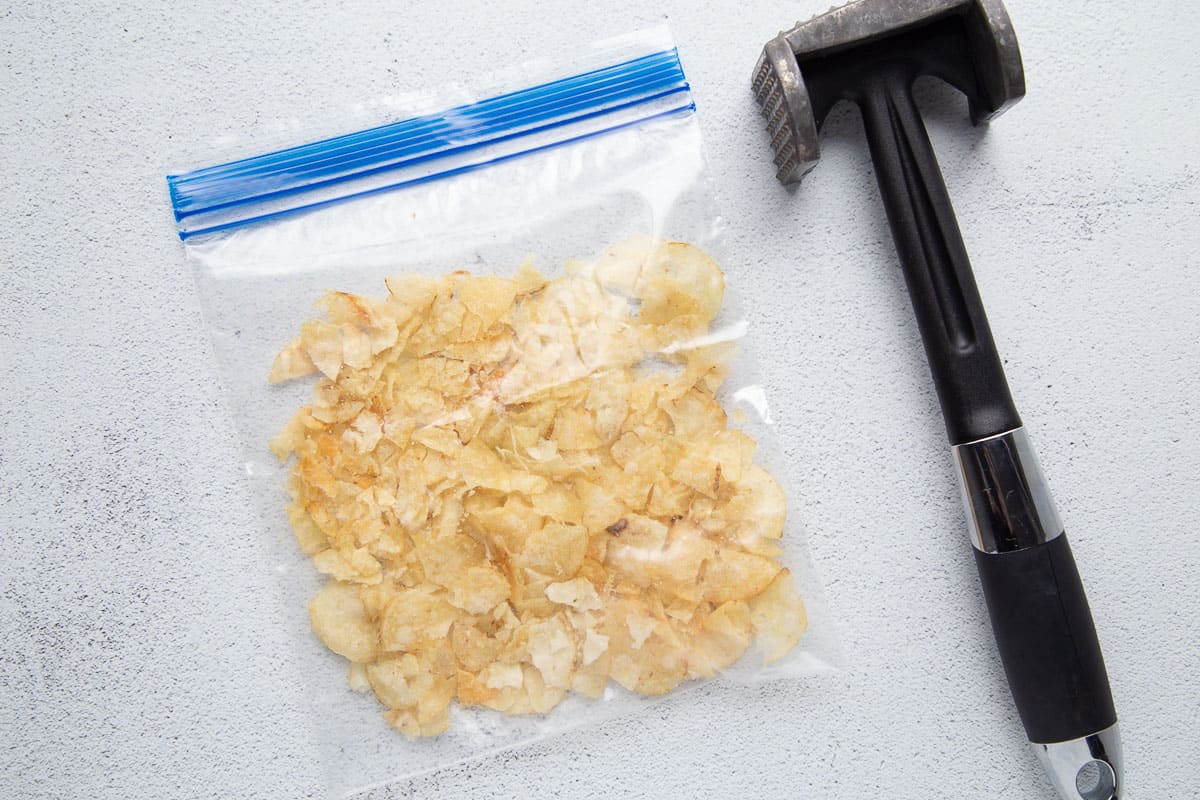 plastic bag full of potato chips next to a meat mallet.