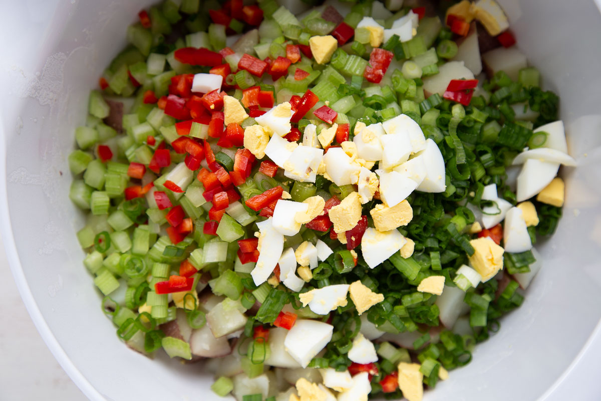 hard boiled eggs, green onions, potatoes, and celery in a white bowl.