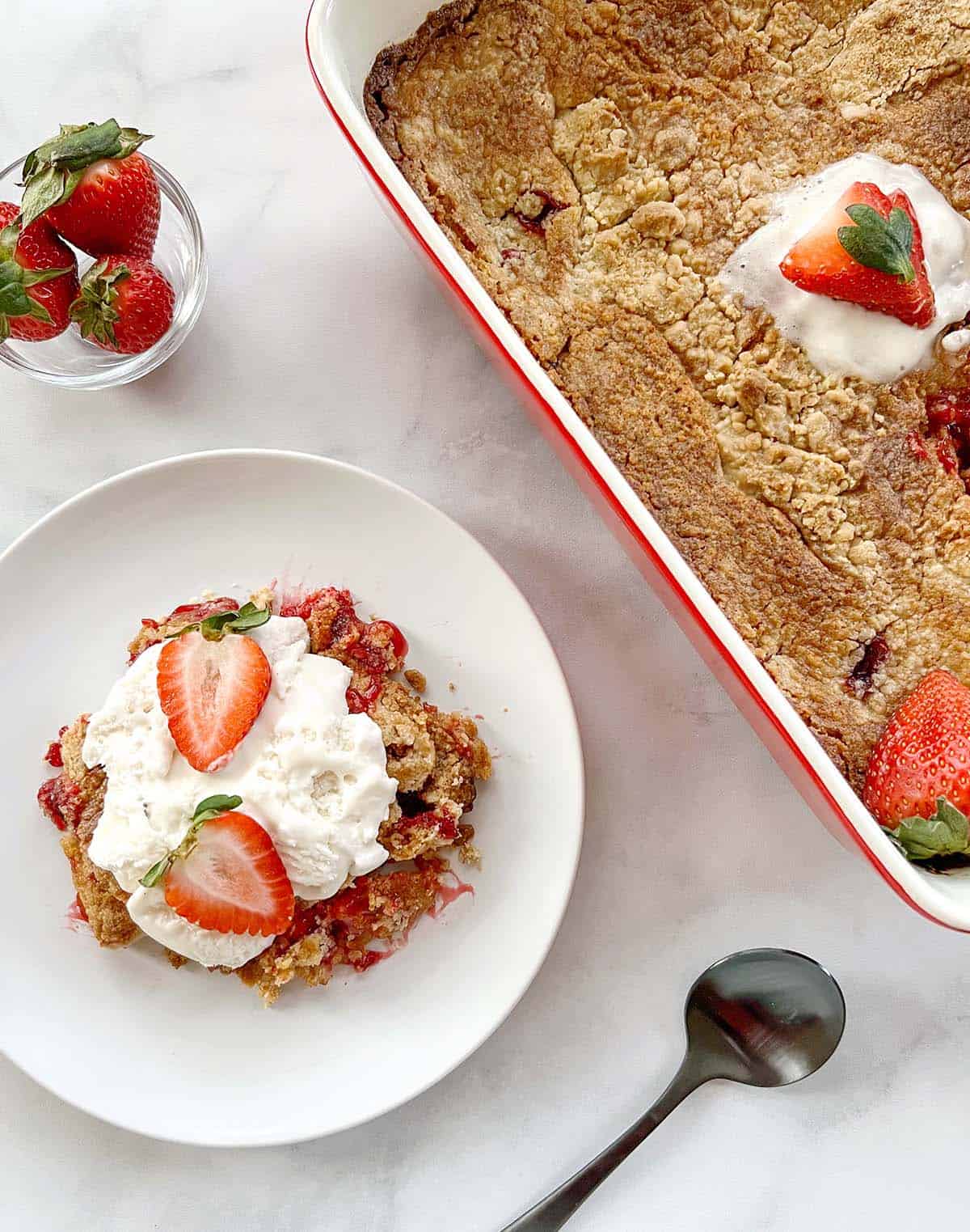 slice of strawberry dump cake on a white plate next to a casserole dish of dump cake.